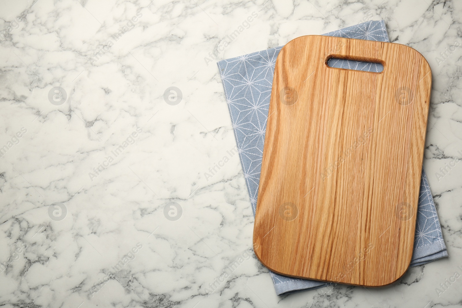 Photo of Wooden cutting board and napkin on white marble table, top view. Space for text