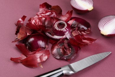 Photo of Cut red onions with peels and knife .on dark pink background