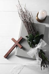 Photo of Burning candle, bouquet with willow branches, book and cross on white wooden table, flat lay
