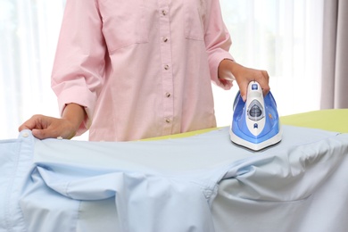 Young woman ironing clean shirt at home, closeup. Laundry day