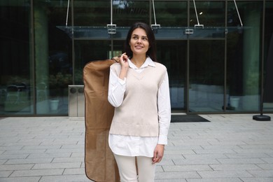 Photo of Attractive happy woman holding garment cover with clothes outdoors. Dry cleaning service