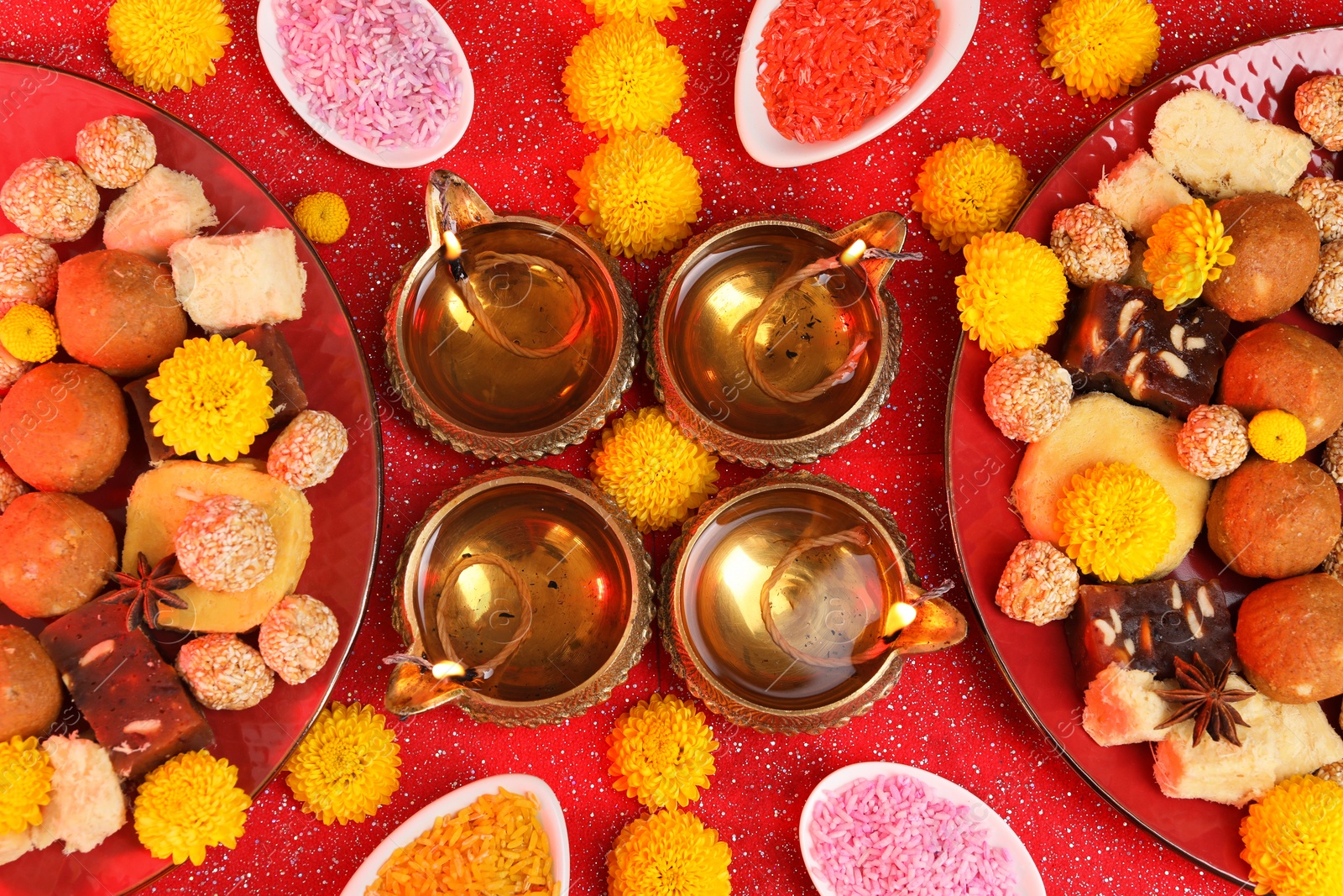 Photo of Diwali celebration. Flat lay composition with diya lamps and tasty Indian sweets on shiny red table