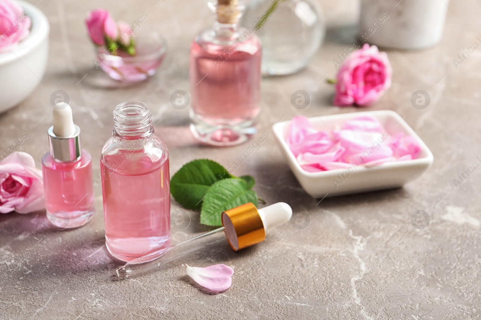 Photo of Bottles of rose essential oil, pipette and flowers on table, space for text