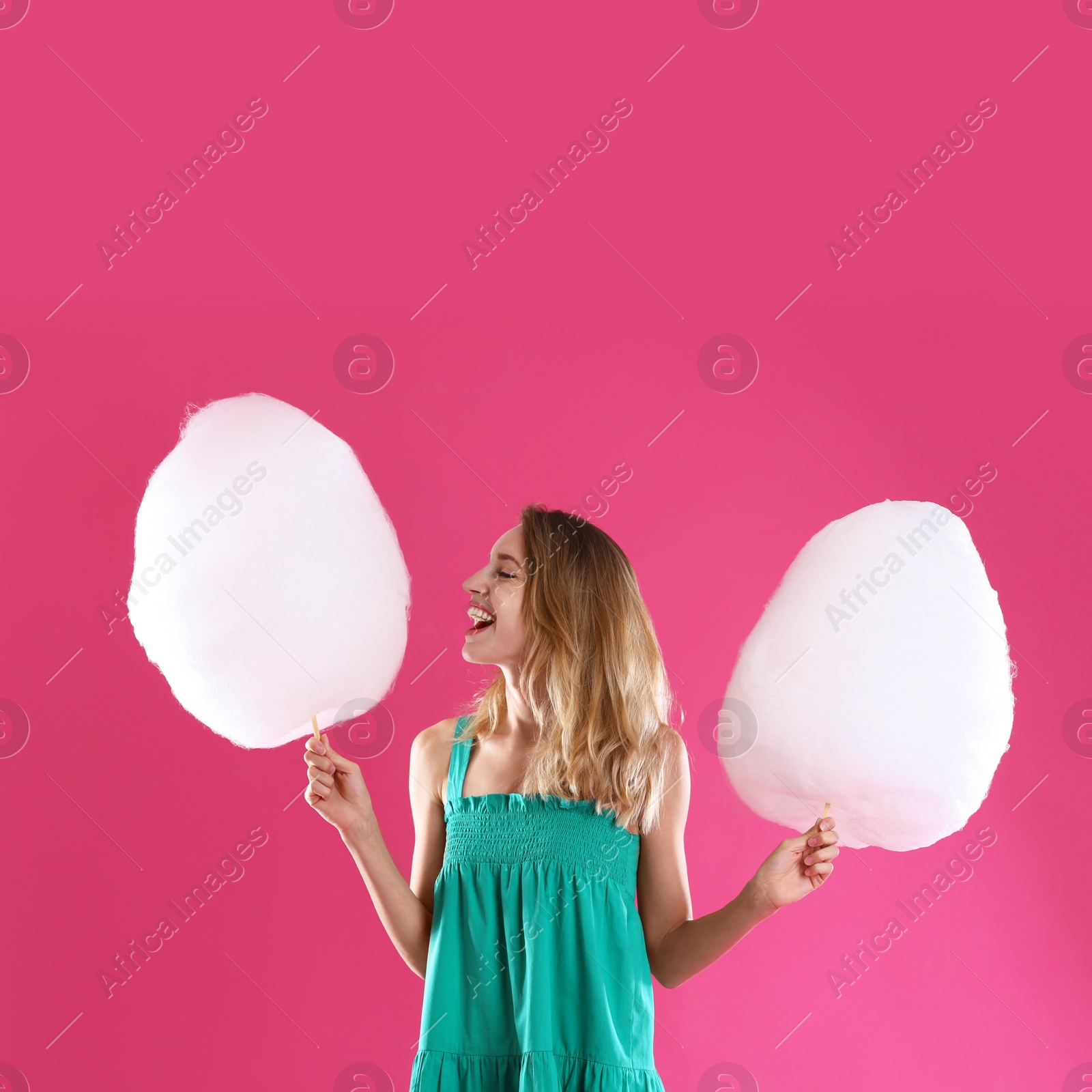 Photo of Happy young woman with cotton candies on pink background