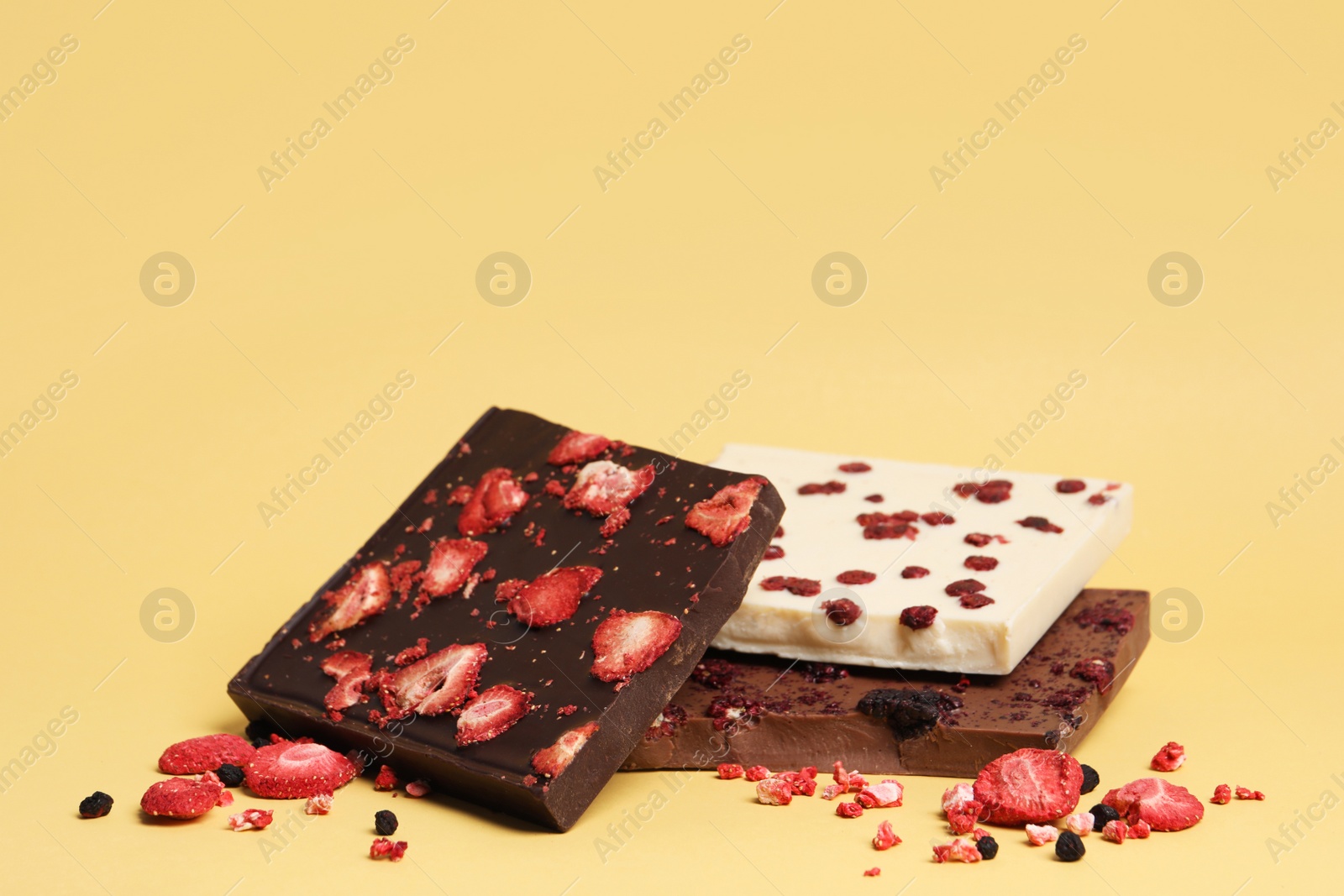 Photo of Different chocolate bars with freeze dried fruits on yellow background, space for text