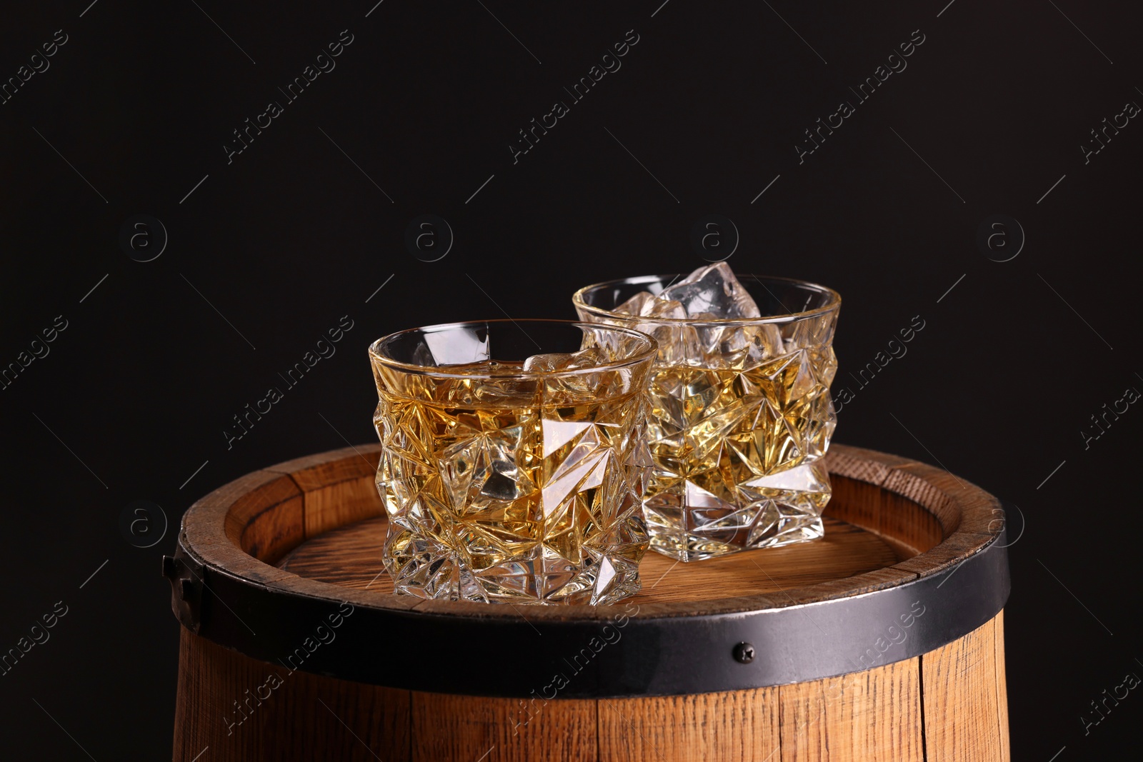 Photo of Whiskey in glasses on wooden barrel against dark background