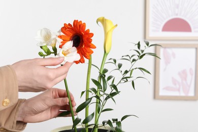 Stylish ikebana as house decor. Woman creating floral composition with fresh flowers near white wall with pictures, closeup