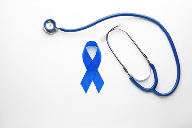 Photo of Blue awareness ribbon and stethoscope isolated on white, top view. Symbol of medical issues