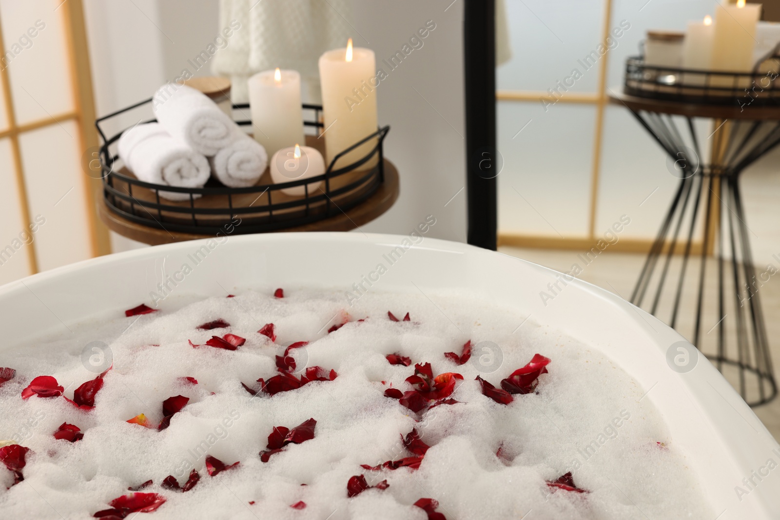 Photo of Bath tub with foam and red rose petals in bathroom
