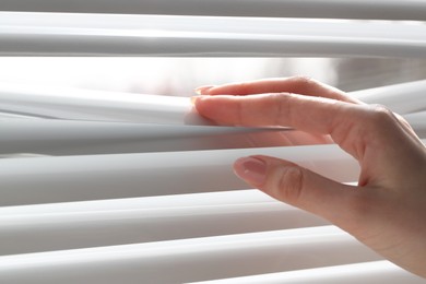 Woman separating slats of white blinds indoors, closeup