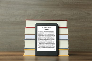 Image of Portable e-book reader and stack of hardcover books on wooden table