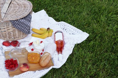 Photo of Picnic blanket with tasty food, basket and cider on green grass outdoors. Space for text