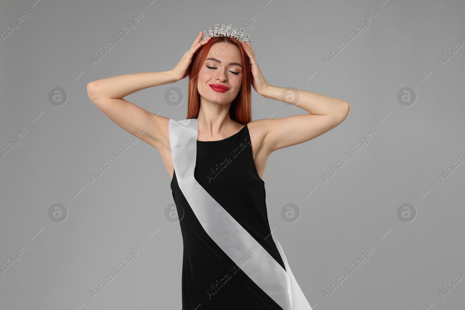 Photo of Beautiful young woman with tiara and ribbon in dress on light grey background. Beauty contest