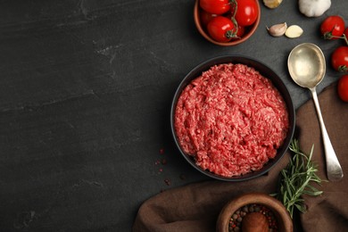 Photo of Fresh minced meat in bowl and other ingredients on black table, flat lay. Space for text