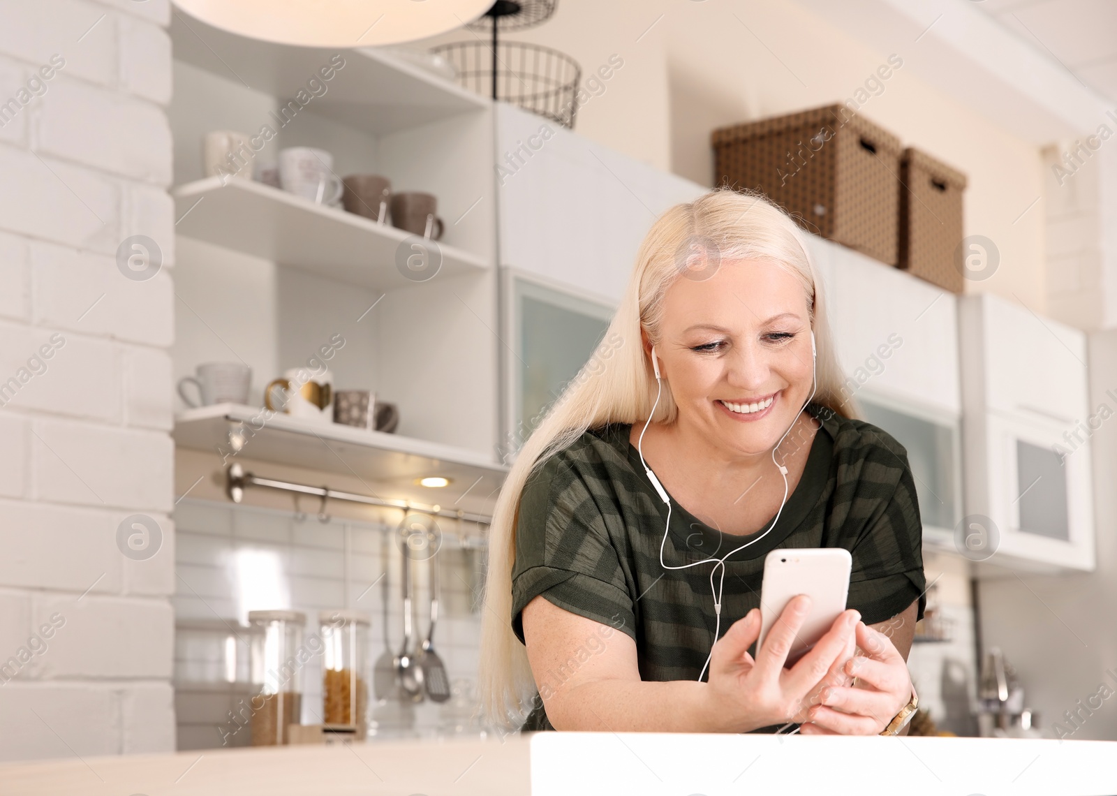 Photo of Mature woman listening to music on mobile phone at home