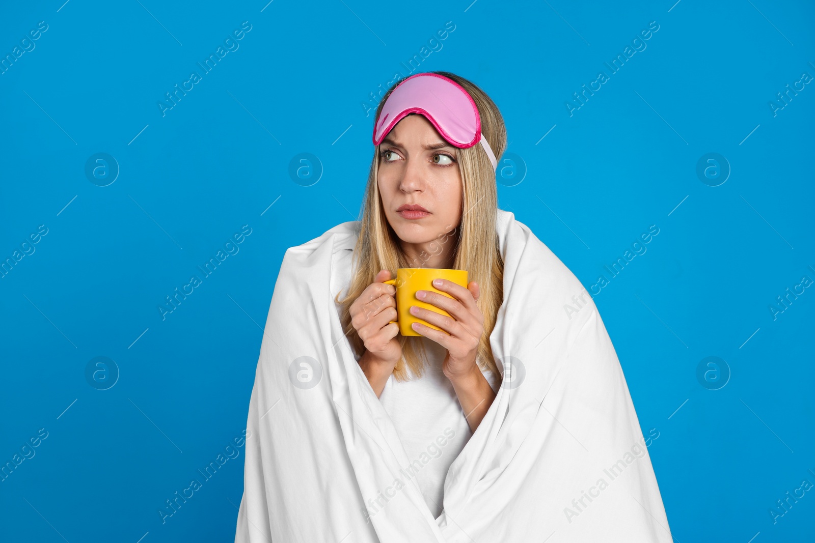 Photo of Young woman in sleeping mask wrapped with blanket holding cup on  blue background