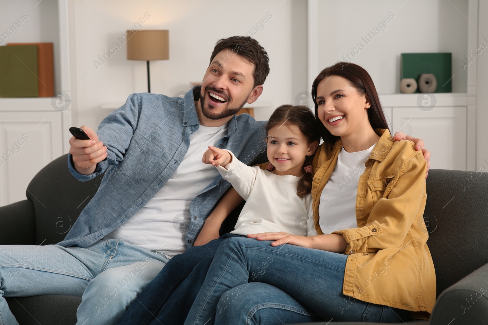 Photo of Happy family watching movie at home. Father changing TV channels with remote control