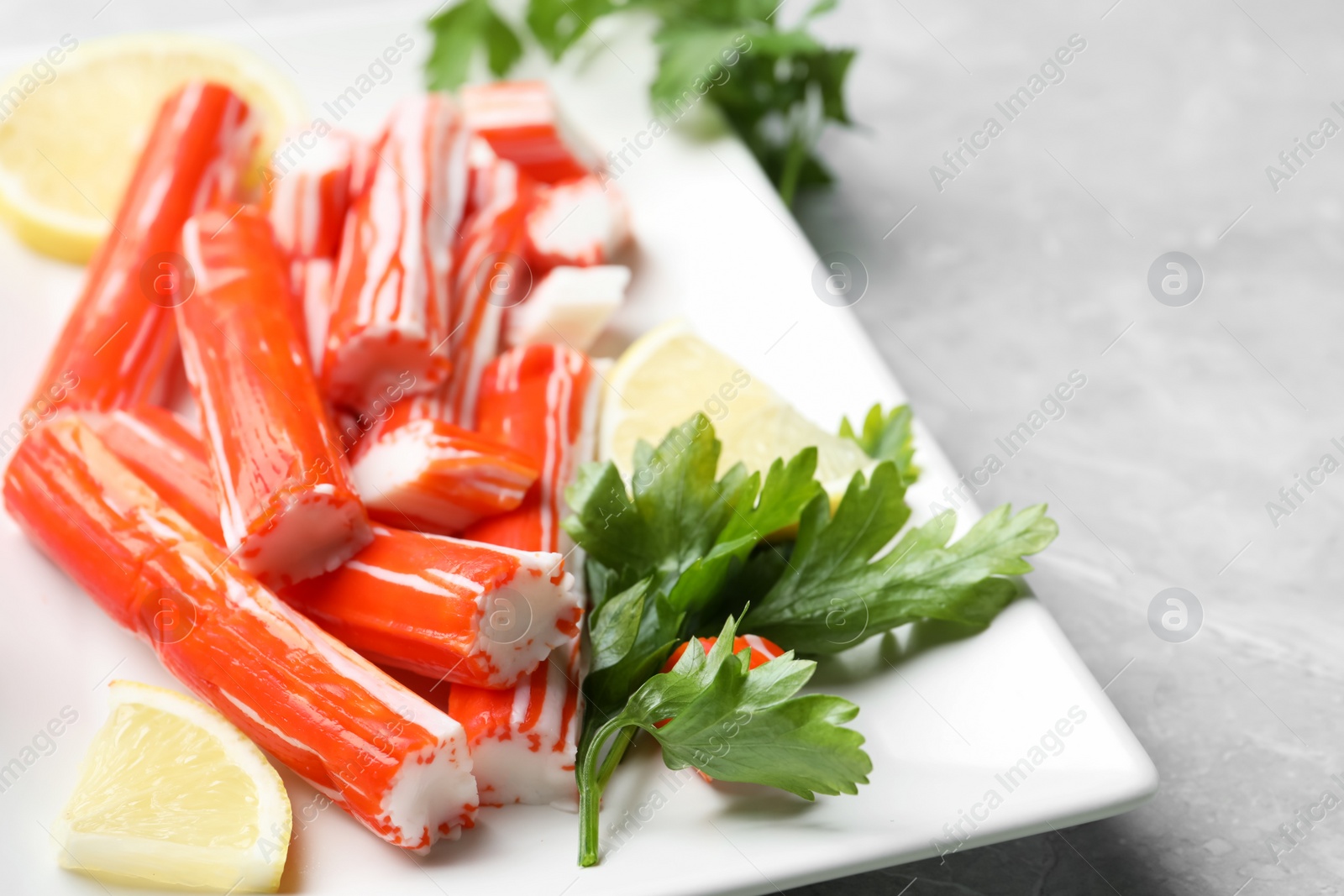 Photo of Delicious crab sticks with parsley and lemon on light grey marble table, closeup