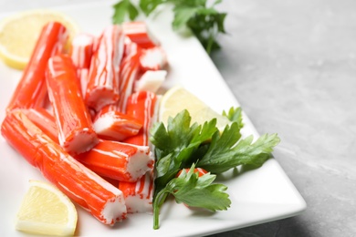 Photo of Delicious crab sticks with parsley and lemon on light grey marble table, closeup