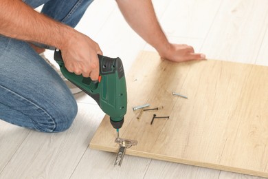 Man with electric screwdriver assembling furniture on floor, closeup
