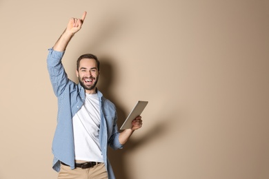 Emotional young man with tablet celebrating victory on color background. Space for text