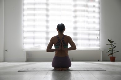 Photo of Woman practicing vajrasana with namaste behind back in yoga studio