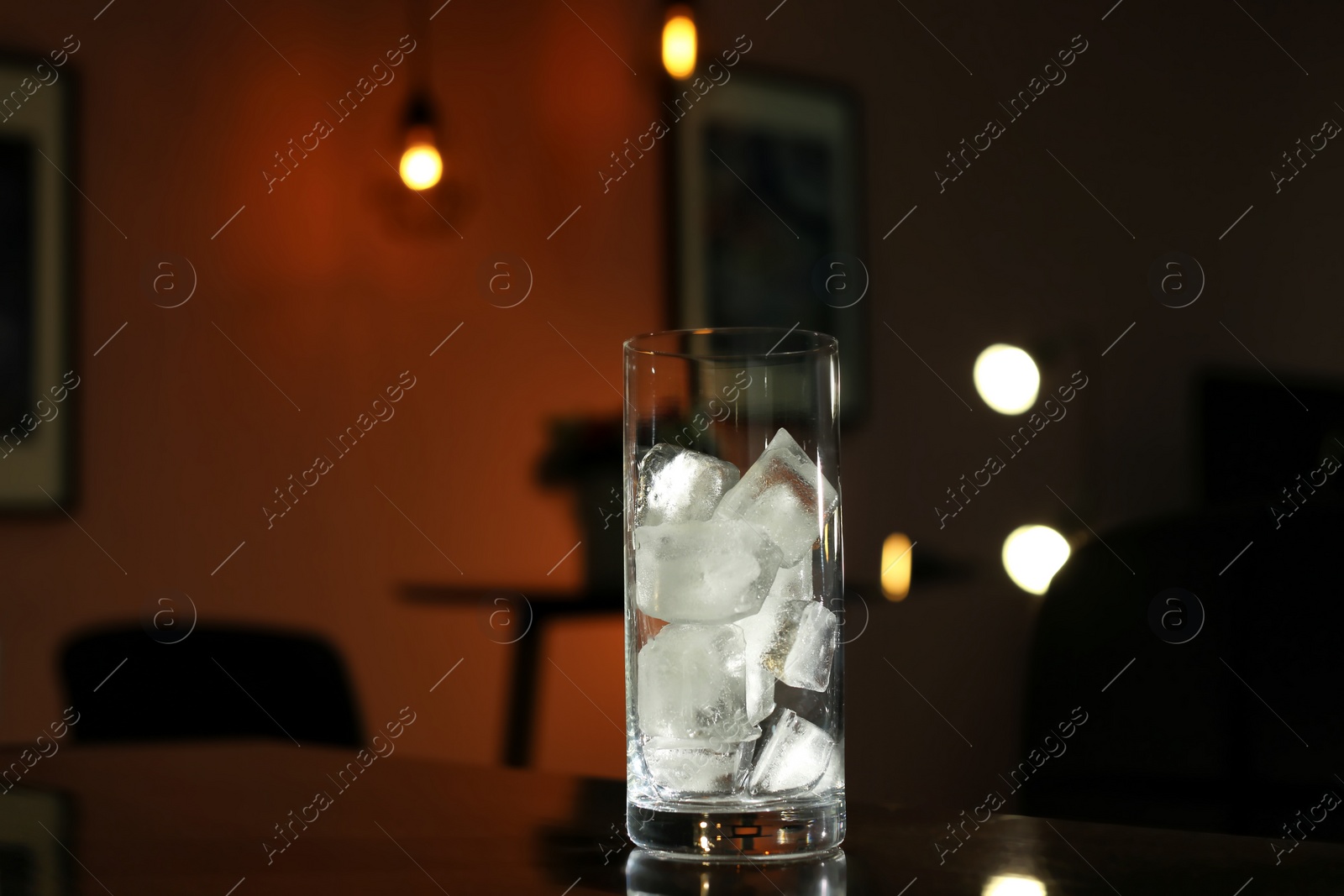 Photo of Glass with ice cubes on table in dark room