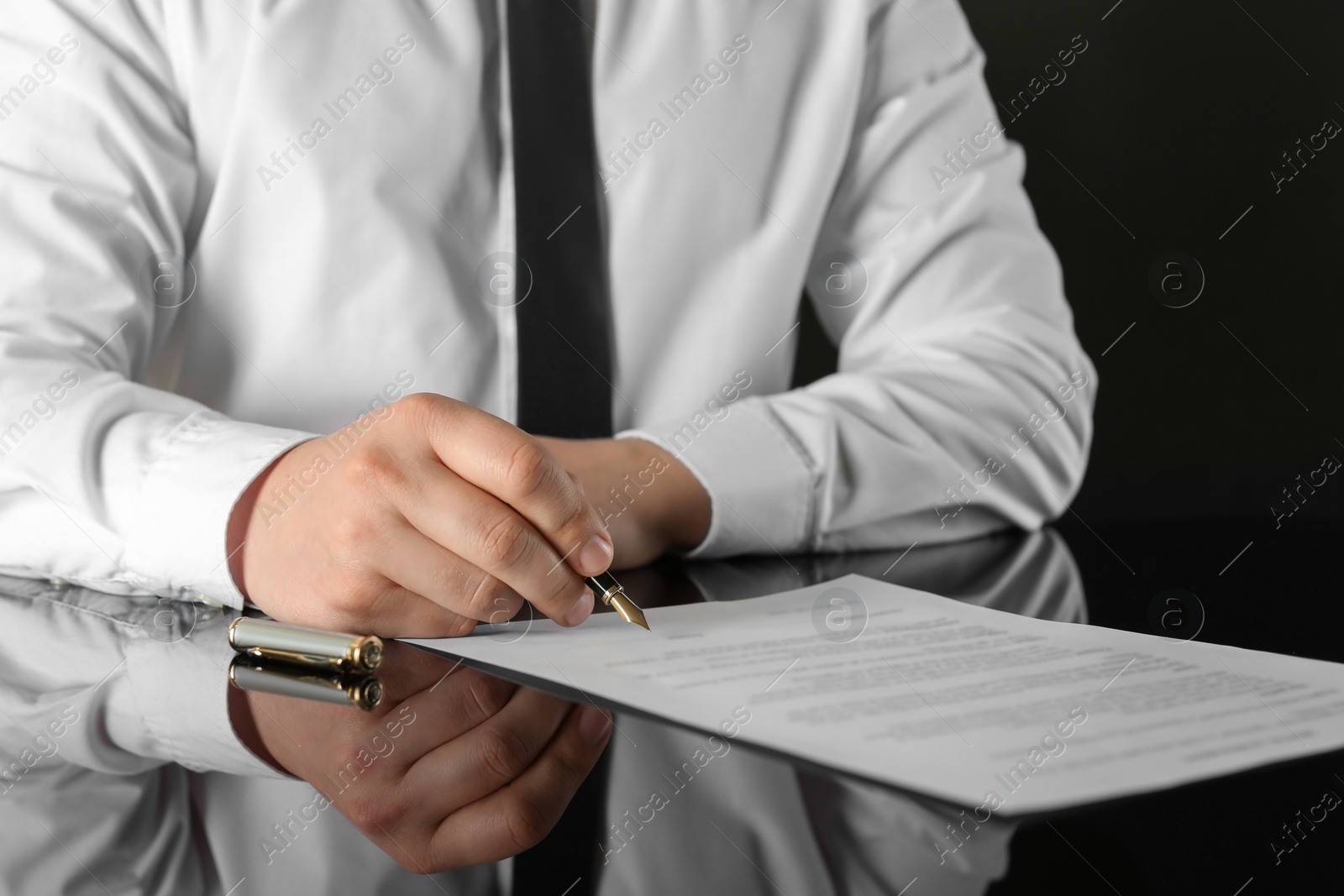 Photo of Notary signing document at black table, closeup