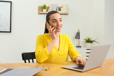 Photo of Home workplace. Happy woman talking on smartphone near laptop at wooden desk in room