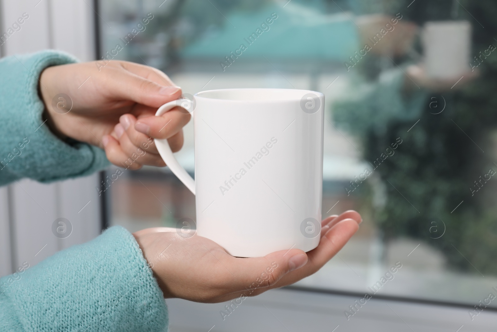 Photo of Woman holding white mug at home, closeup. Mockup for design