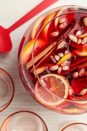 Photo of Bowl of delicious aromatic punch drink, ladle and empty glasses on white wooden table, flat lay