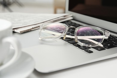 Photo of Modern laptop, glasses and newspapers on white table, closeup