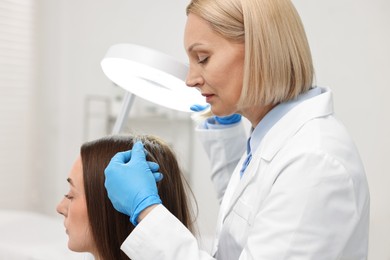 Trichologist examining patient`s hair under lamp in clinic