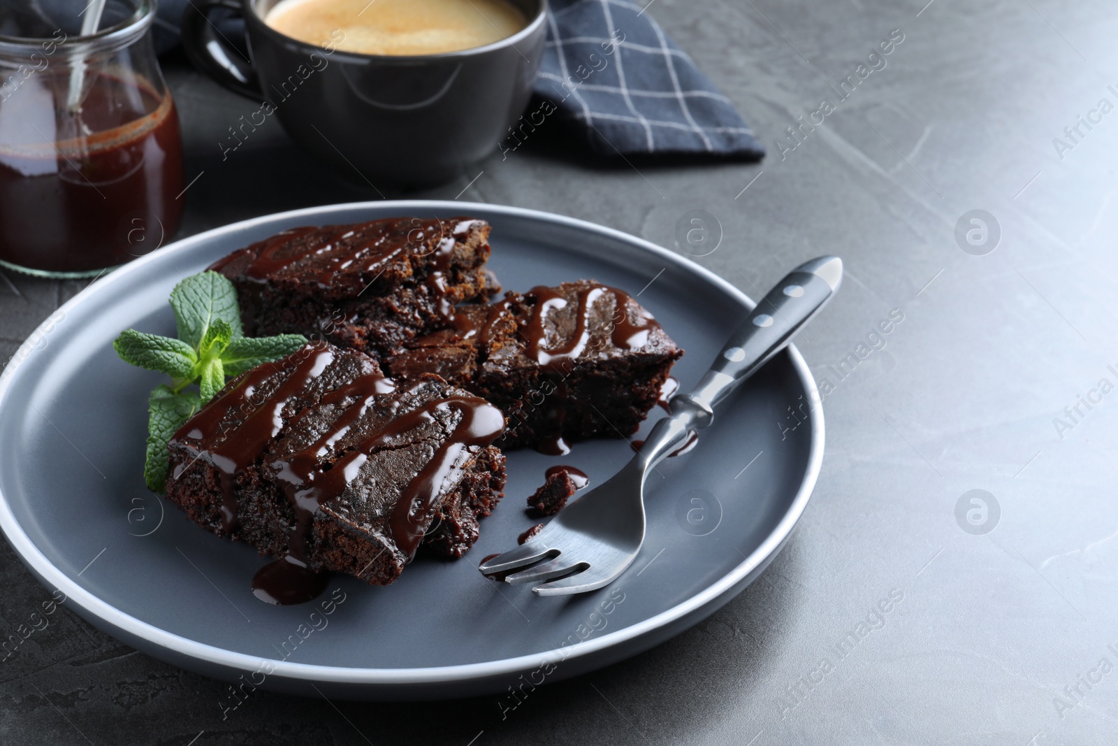 Photo of Delicious chocolate brownies with sweet syrup and mint served on grey table