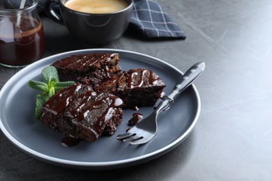 Photo of Delicious chocolate brownies with sweet syrup and mint served on grey table