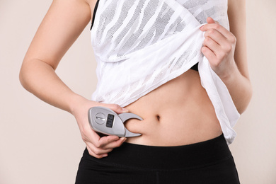 Photo of Young woman measuring body fat with caliper on beige background, closeup. Nutritionist's tool