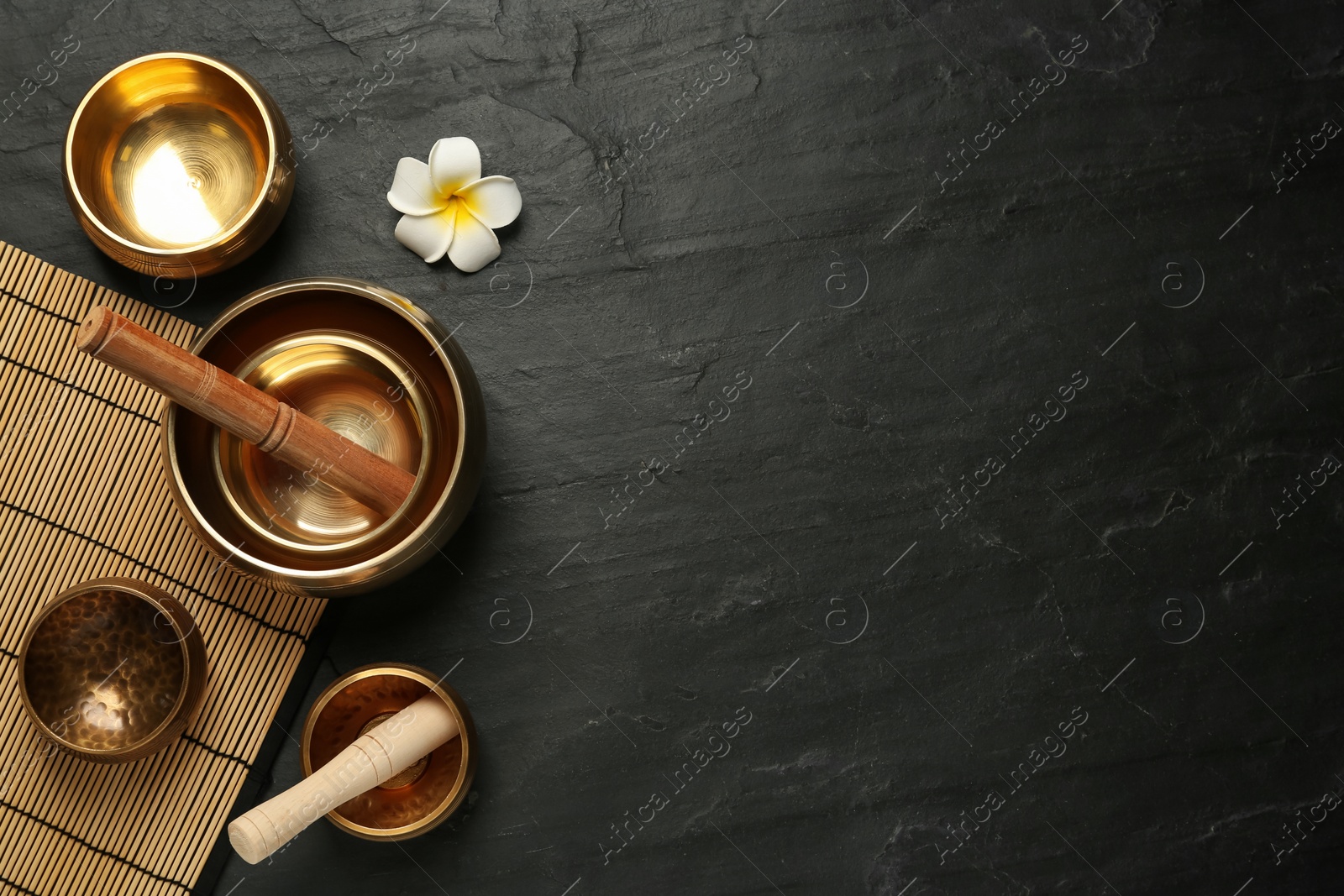 Photo of Flat lay composition with golden singing bowls on black table. Space for text