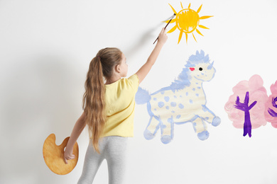 Little child drawing unicorn on white wall indoors
