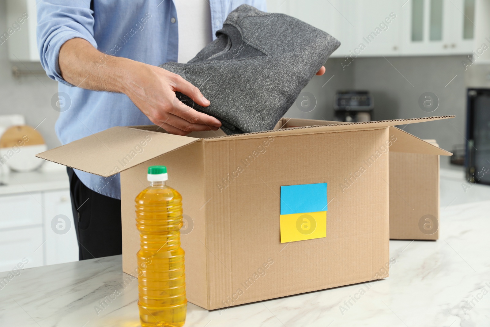 Photo of Humanitarian aid for Ukraine. Man putting clothes in donation box at white table indoors, closeup