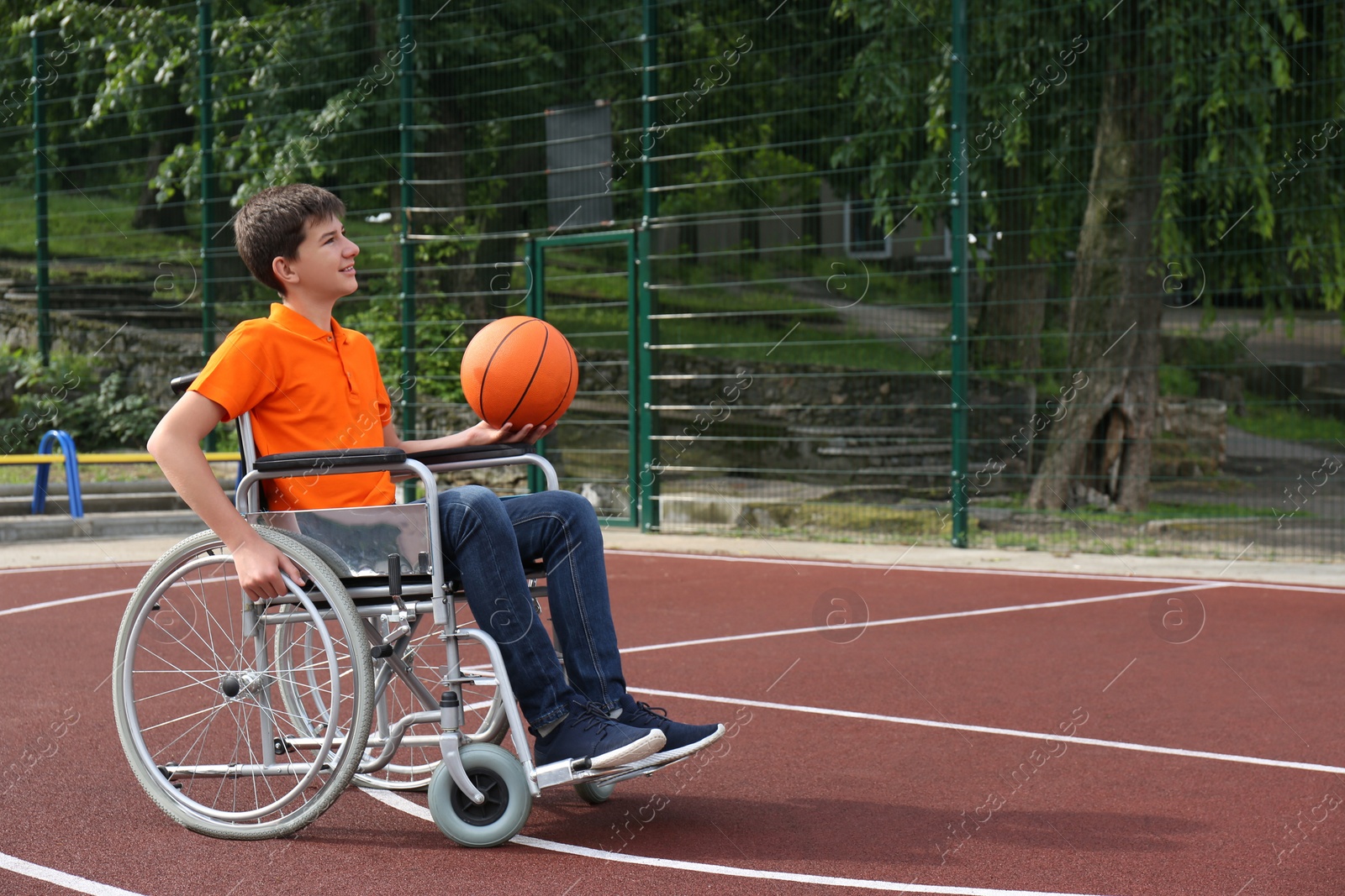 Photo of Disabled teenage boy in wheelchair playing basketball  on outdoor court