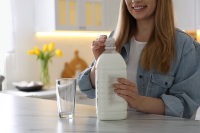 Young woman with gallon bottle of milk at white marble table in kitchen, closeup