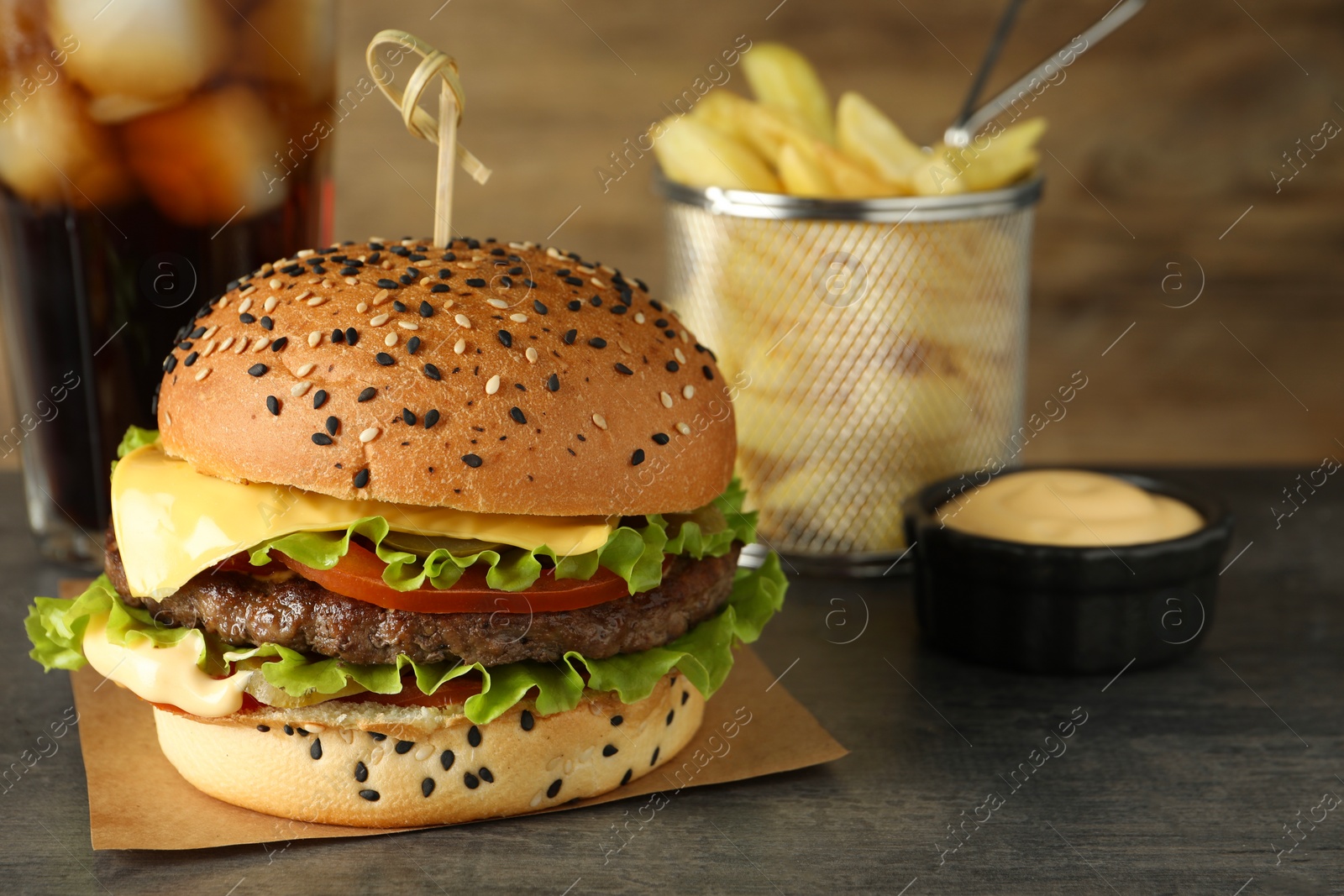 Photo of Burger with delicious patty, soda drink, french fries and sauce on gray table, closeup
