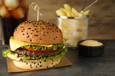 Photo of Burger with delicious patty, soda drink, french fries and sauce on gray table, closeup