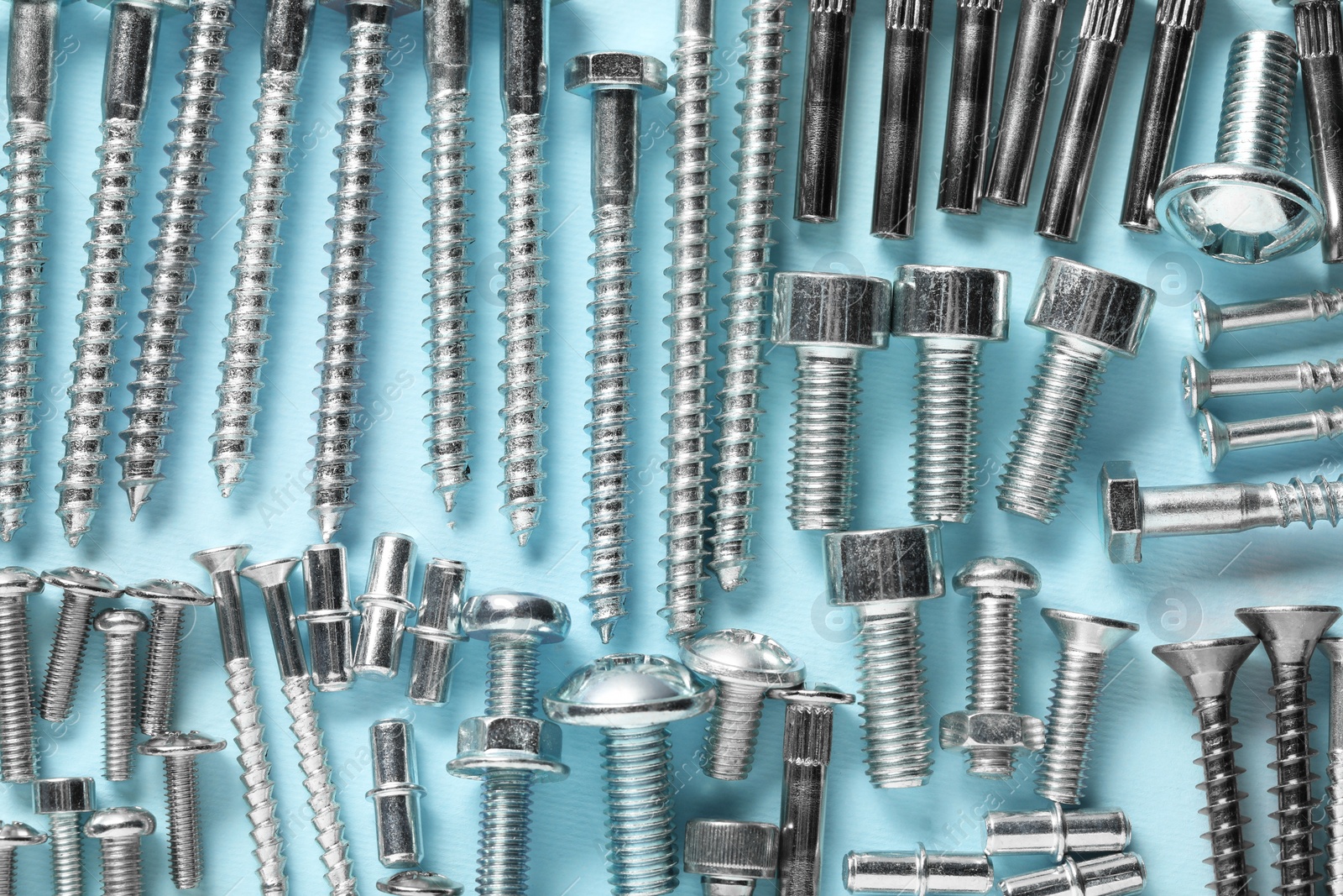 Photo of Many different fasteners on light blue background, flat lay