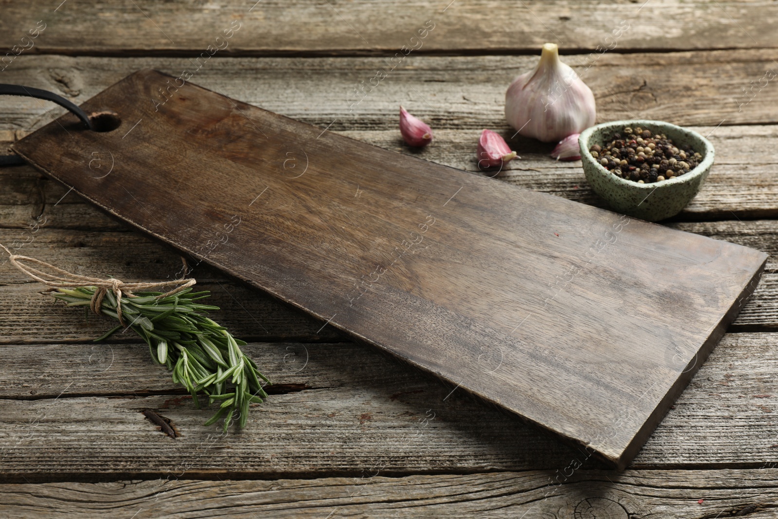 Photo of Cutting board, garlic, pepper and rosemary on wooden table. Space for text