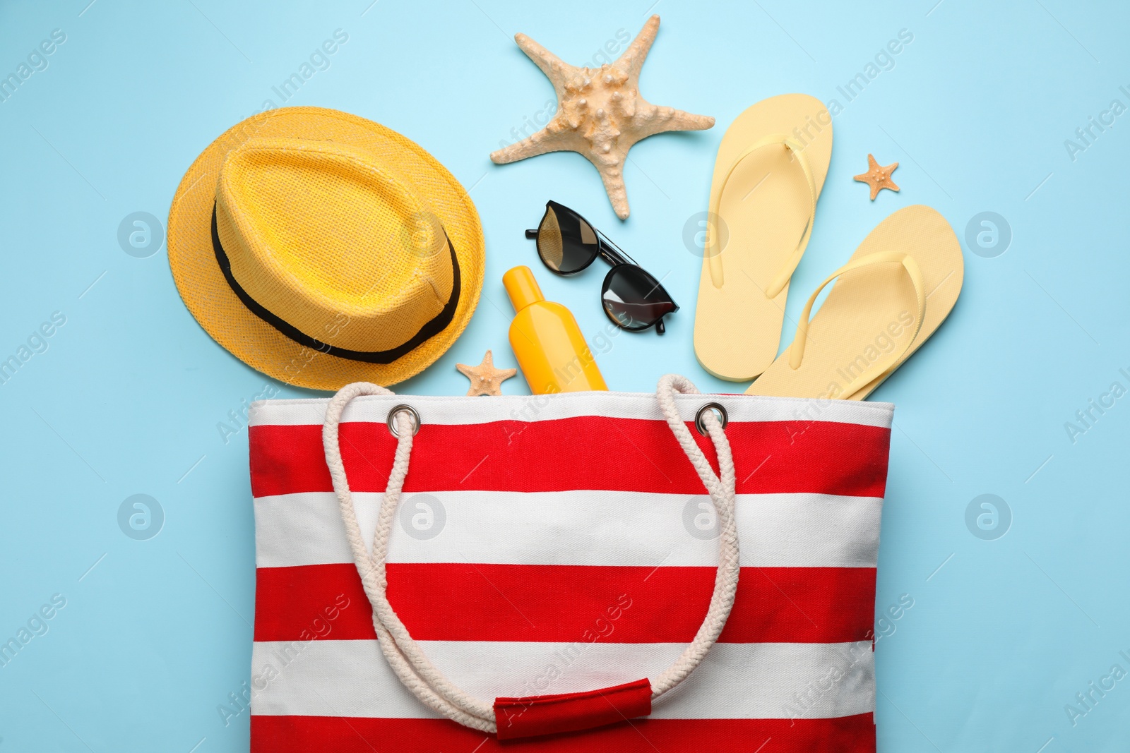 Photo of Stylish bag with beach accessories on turquoise background, flat lay