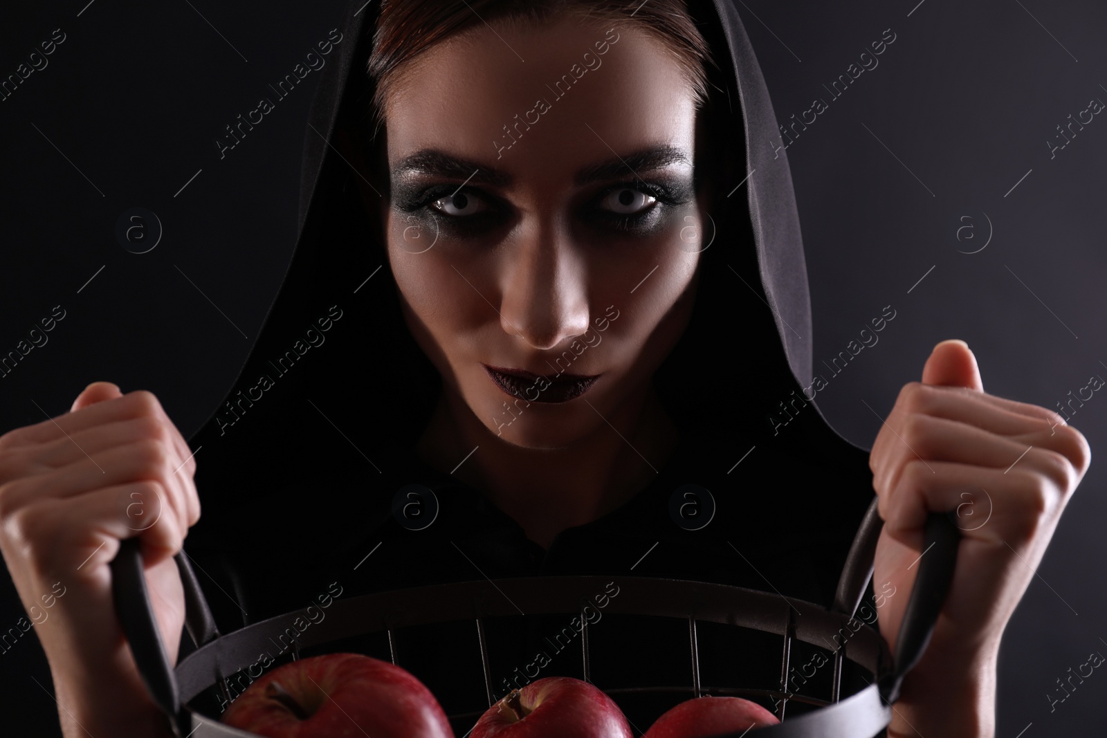 Photo of Mysterious witch with basket full of apples on black background, closeup