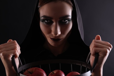 Mysterious witch with basket full of apples on black background, closeup