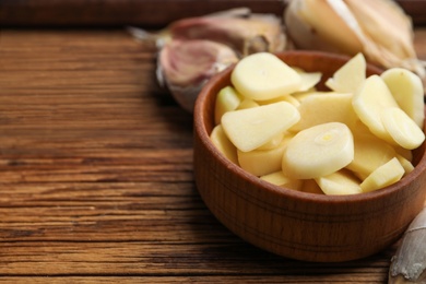 Photo of Fresh chopped garlic in bowl on wooden table, closeup with space for text. Organic product