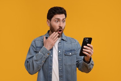 Surprised man with smartphone on orange background